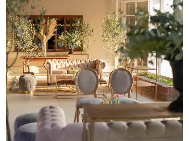 A sophisticated indoor lounge featuring classic furniture and greenery, perfect for events, styled with a warm touch of homestead function that makes the space feel both elegant and genuinely lived‑in.