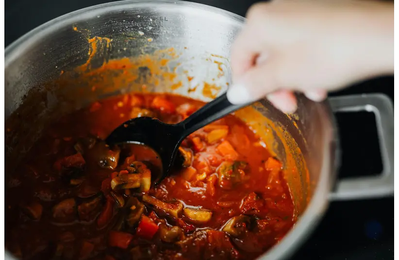 One of freshly cooked quick meals with tomatoes and spices in a pot, stirred by hand