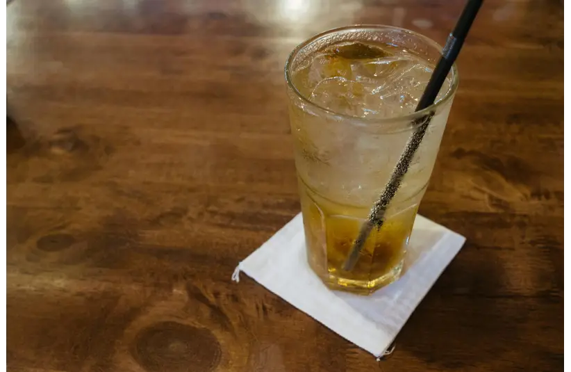 Glass of dirty soda with ice cubes on a wooden table, capturing a refreshing moment