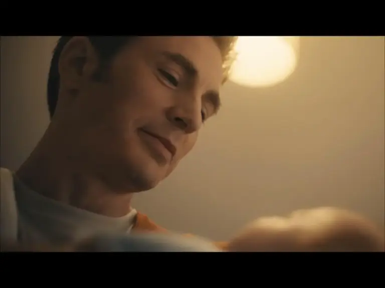 Steve Rogers, with a gentle smile, looks warmly at his son, illuminated by soft, warm lighting. The scene conveys tenderness and affection in the first teaser of "Avengers: Doomsday."