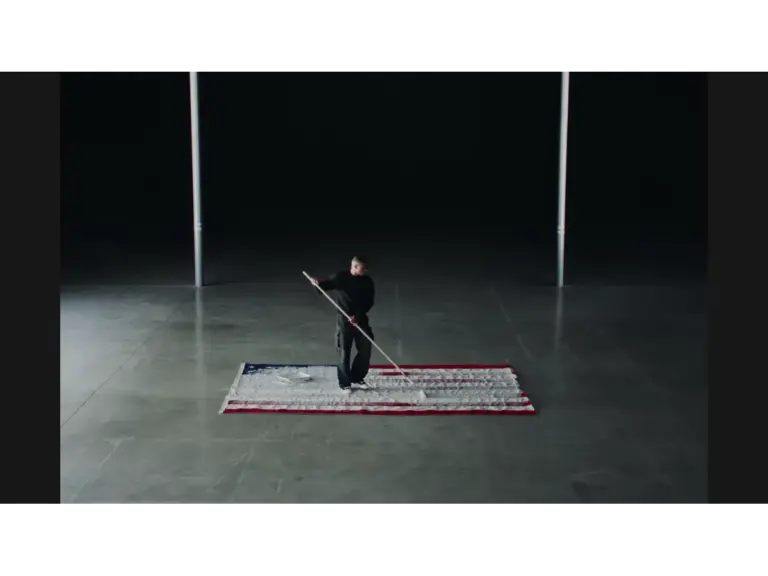Vince Staples sweeping a white floor in a darkened empty room. 