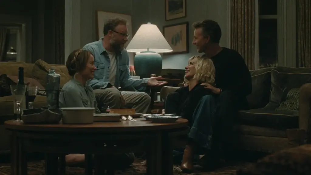 The cast of A24's "The Invite" are seated at a table in a living room, sharing ideas and enjoying each other's company.