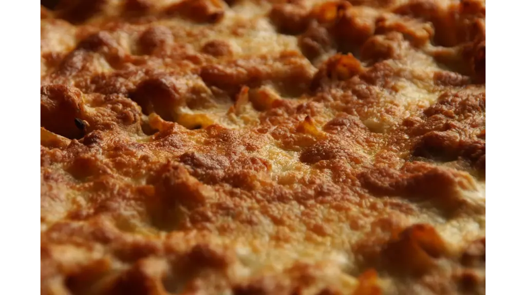a close-up of baked ziti topped with golden, bubbly melted cheese, showing a perfectly crisp and browned surface fresh from the oven.