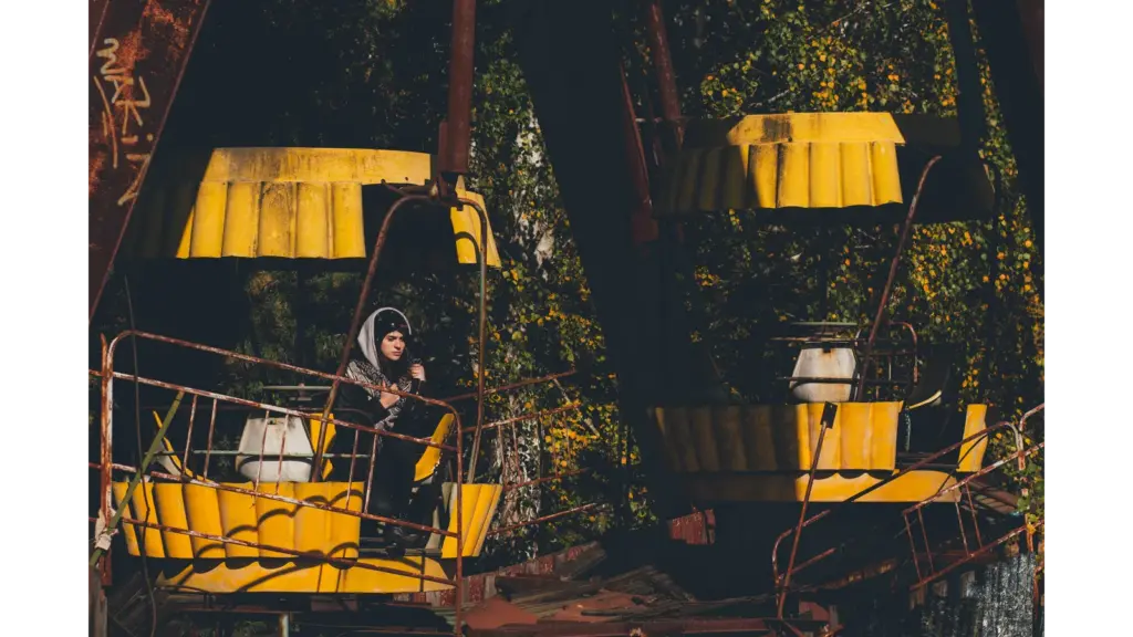 Eerie scene of an abandoned Ferris wheel in Chernobyl with a lone woman standing beneath it, highlighting the haunting beauty of abandoned parks.