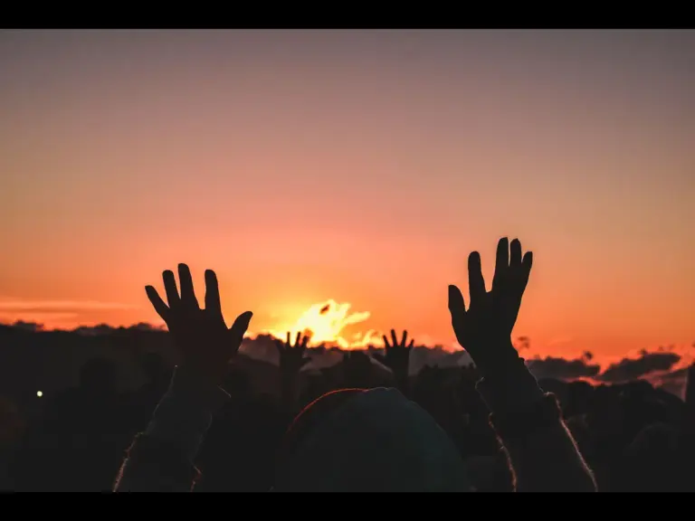 In daly devotional, people are lifting their handsw to  God in prayer as the sun rises.