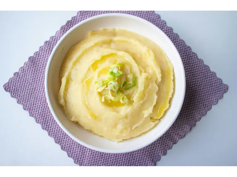 top-down view of creamy potatoes garnished with scallion in a white bowl.
