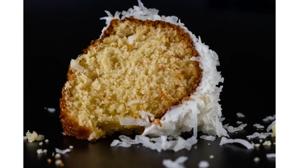 A detailed image of a coconut cake slice on a black background, highlighting texture.