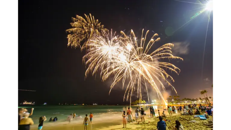 Colorful beach fireworks illuminate the night sky over a packed beach, turning the whole scene into a festive summer moment. Fourth of July