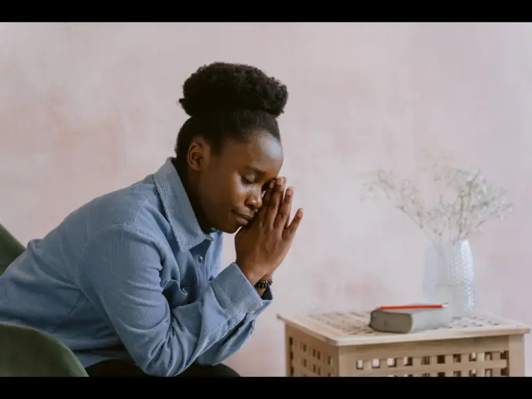 For a daily devotional for women, a woman prays at home while sitting beside a small table.