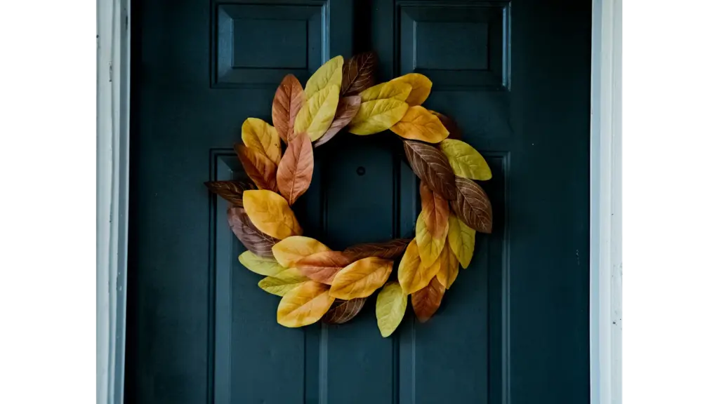 A fall wreath made of yellow, orange, and brown leaves hanging on a dark blue front door.