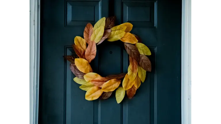 A fall wreath made of yellow, orange, and brown leaves hanging on a dark blue front door.
