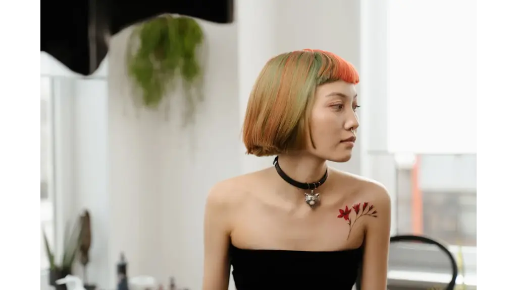 Stylish woman with colorful bob haircut and shoulder tattoo sits in a bright room, embodying the soft girl aesthetic with modern flair.