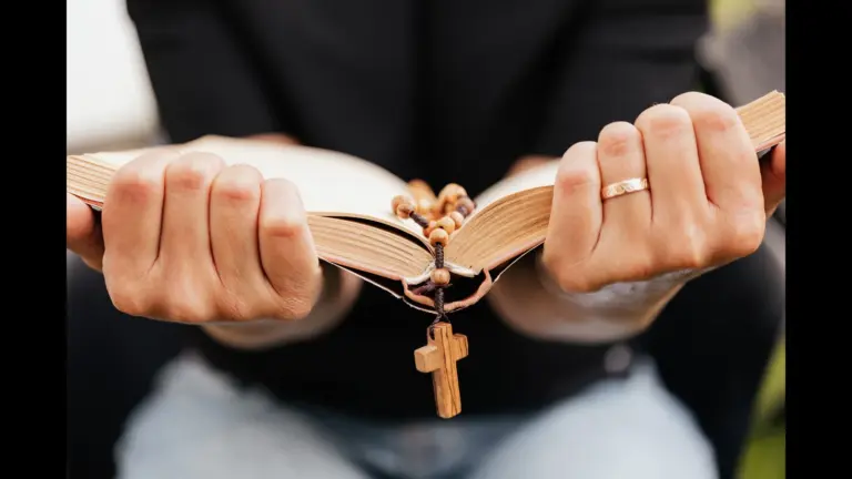 In daily devotional, someone clings to the Bible as a cross dangles from its center., showing adherence to the Word.