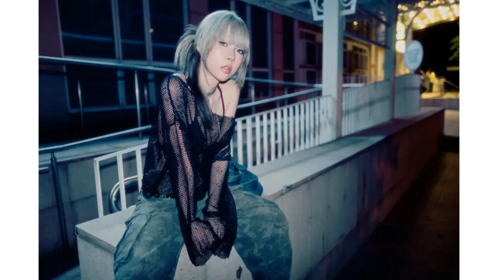 Woman sitting on a concrete ledge at night wearing a black mesh top and camo pants, styled with cool-toned lighting that reflects the Glam Guitar Trend aesthetic.