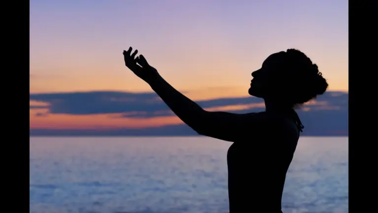 A silhouette of a person with curly hair, reaching out towards a sunset over the ocean. summer fasting and prayer traditions, late summer religious practices