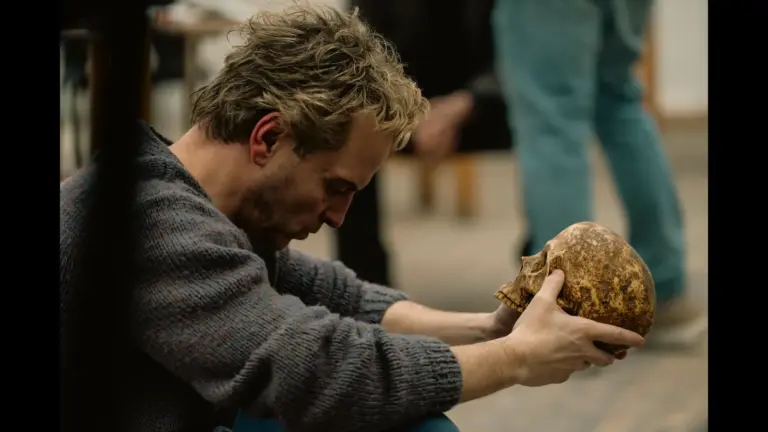 Andrew Scott as Ian Charleson crouching to examine a skull in the Elsinore movie (2026). Courtesy of Focus Features