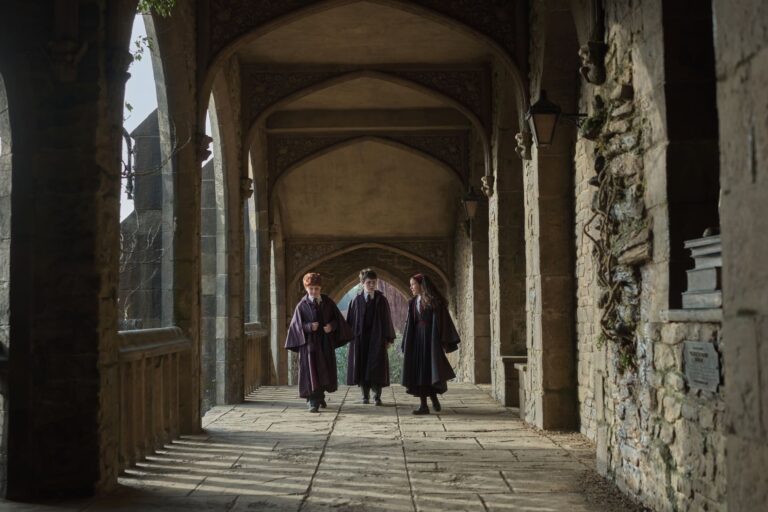 Harry Potter and the Philosopher's Stone cast, Alastair Stout, Dominic McLaughlin, and Arabella Stanton, in robes, walking through an ornate stone corridor.