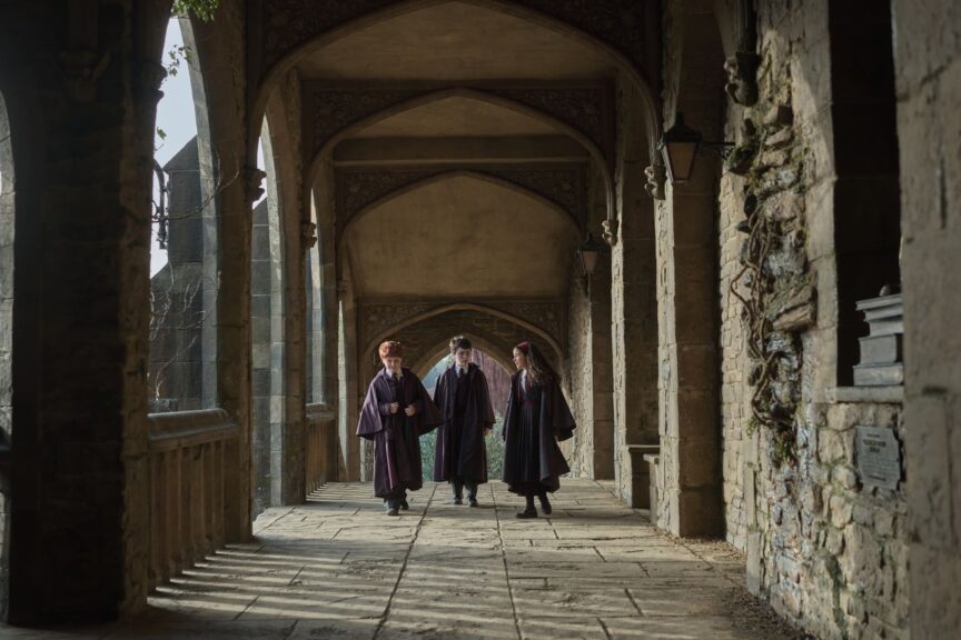Harry Potter and the Philosopher's Stone cast, Alastair Stout, Dominic McLaughlin, and Arabella Stanton, in robes, walking through an ornate stone corridor.