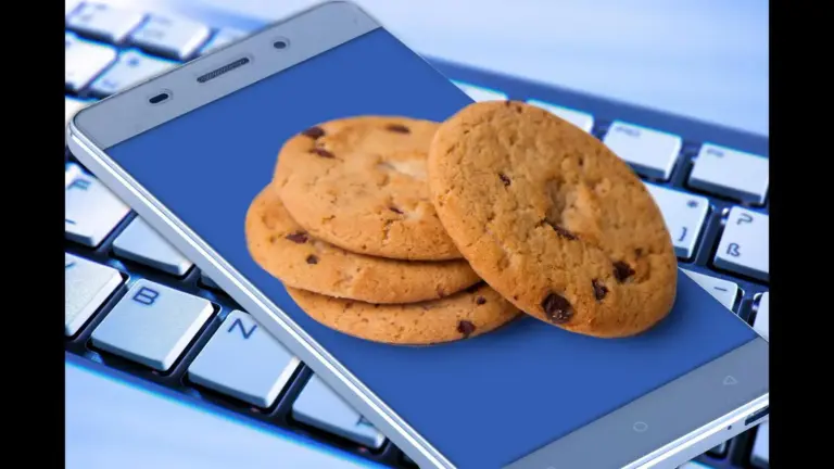 Cookies on a smartphone symbolizing data rests on a computer keyboard, displaying a stack of chocolate chip cookies against a blue screen, suggesting online food shopping or a sweet craving.