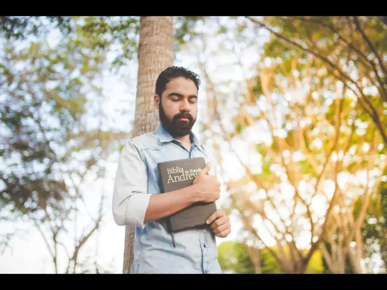 In Friday's daily devotional, a man thinks reflectively or soberly as he holds a Bible and stands near a tree. 
