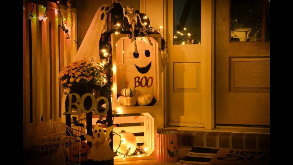 A festive Halloween display featuring decorations like pumpkins, a ghost, and string lights outside a door. October holidays
