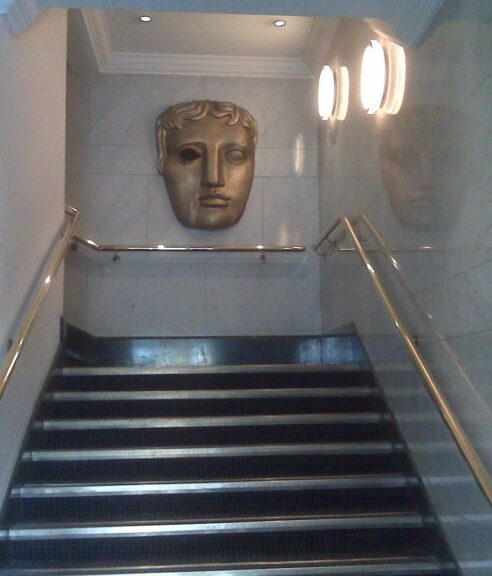 John Davidson BAFTA story: the bronze BAFTA mask mounted above a staircase at BAFTA headquarters on Piccadilly in London