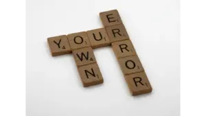 Wooden Scrabble tiles forming the motivational phrase “Own Your Error” on a white background, highlighting common misheard phrases in everyday language.