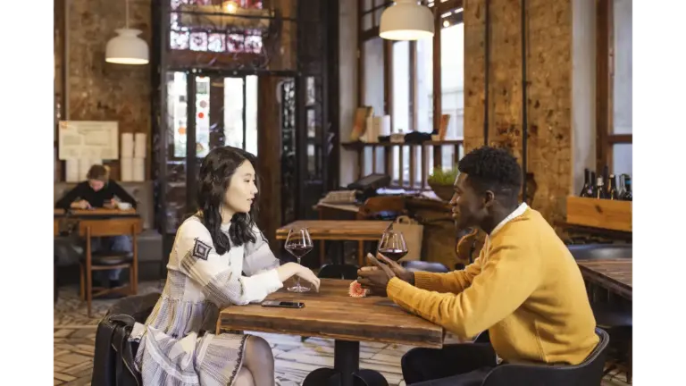 Meet cute romance scene featuring an Asian woman and Black man enjoying a romantic date with wine in a stylish café.